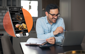 בעל עסק בחולצה מכופתרת כחולה יושב ורואה איך להגדיל הכנסות באמצעות אפליקציית הזמנות ומשווה ברשומות שלו על קליפבורד